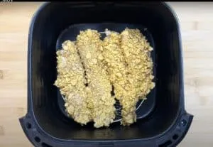 Cornflake-crusted chicken tenders in an air fryer basket, ready to cook. Perfect crispy homemade recipe.